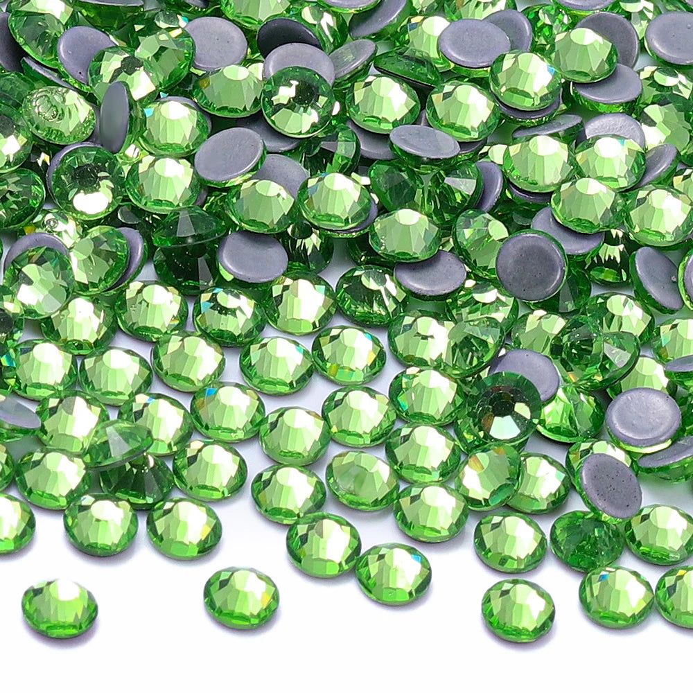 A close-up view of green glass crystal hot fix rhinestones and silver accents scattered on a white background.