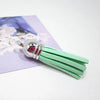 Silver velvet tassels with green fibers displayed on a purple card.