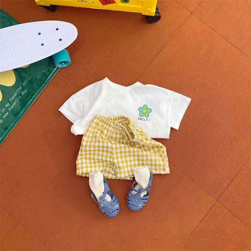 A yellow gingham shirt and blue patterned shorts set laid on an orange surface.