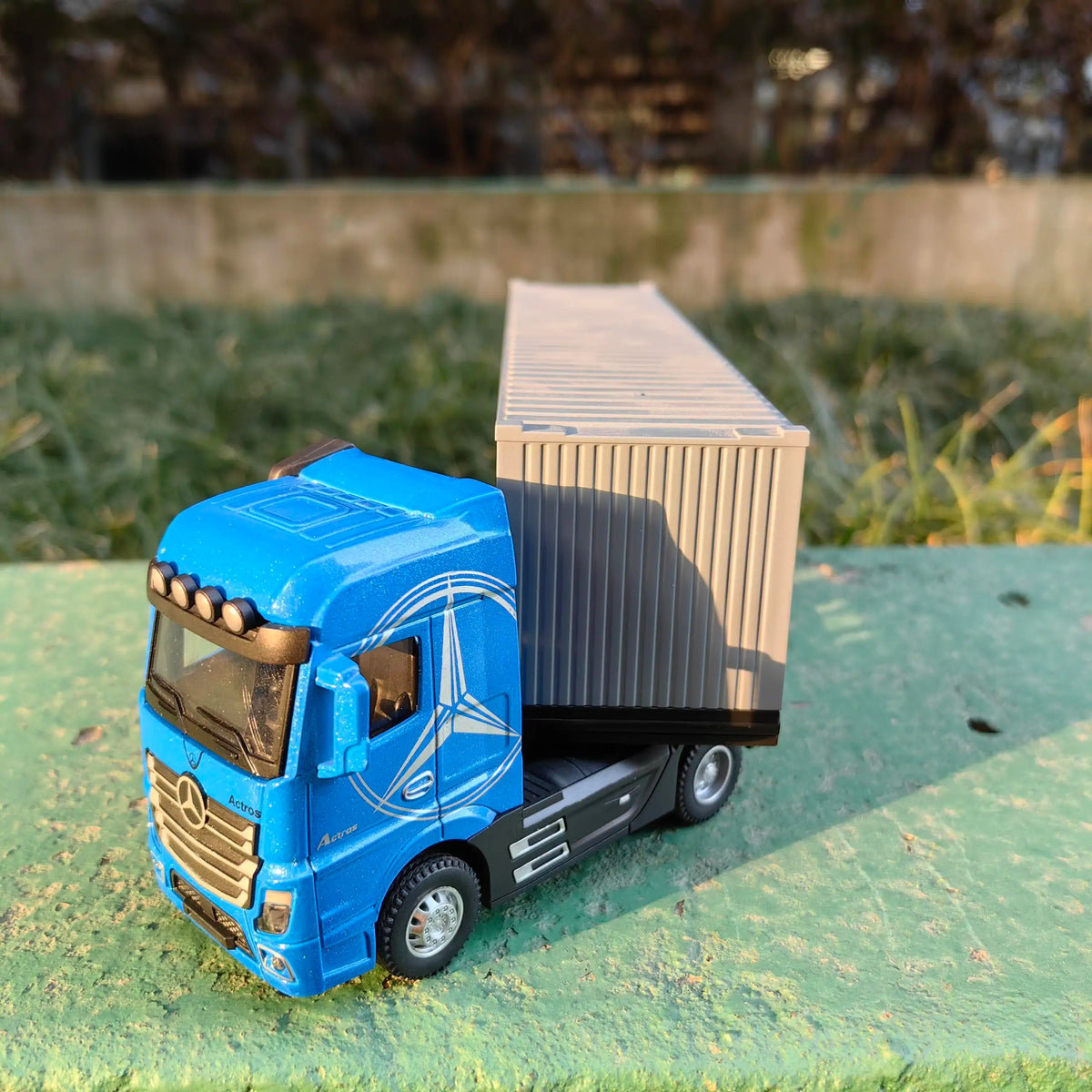 A blue 1:50 scale diecast model of a container truck with lights and sounds parked on green grass.