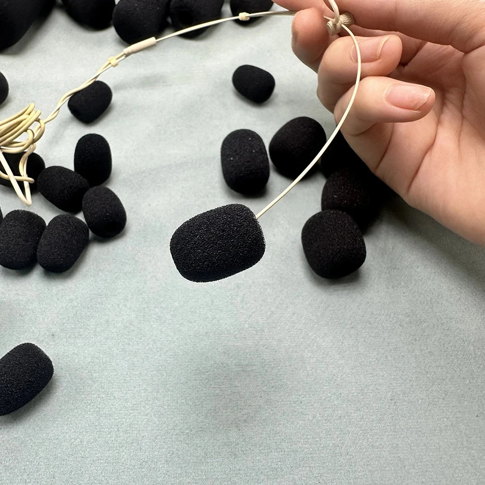 A hand holds a thin wire with black foam covers, showing replacement microphone foam for meeting microphones.
