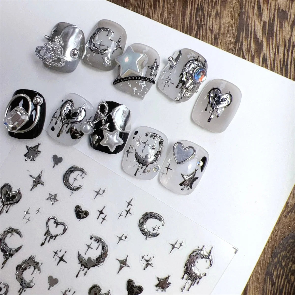A collection of silver and black gothic nail art stickers featuring stars, moons, and hearts on a white background.