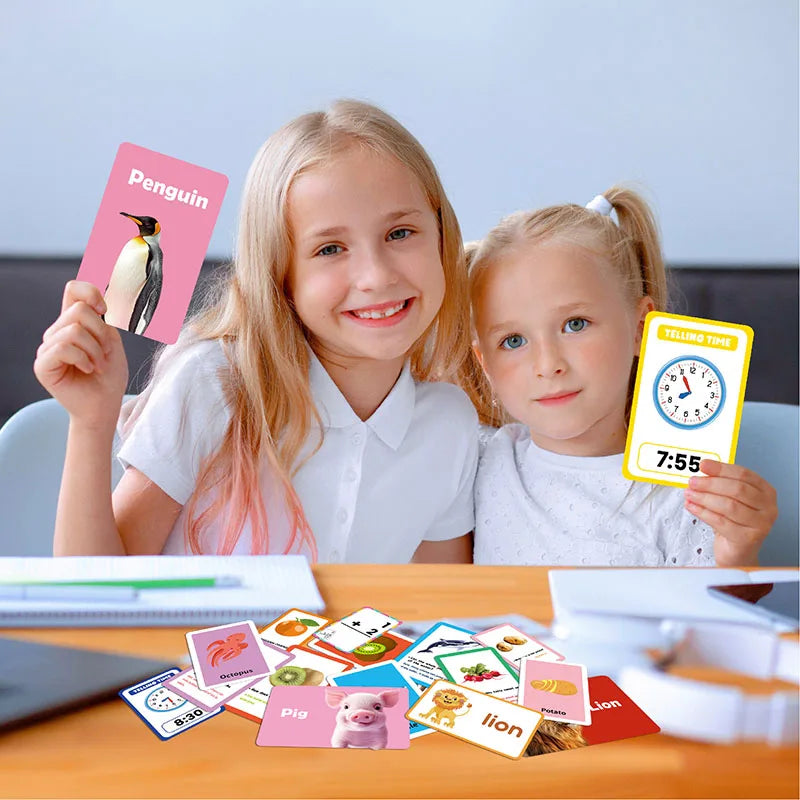 Two young girls holding colorful flash cards featuring animals and shapes for early learning