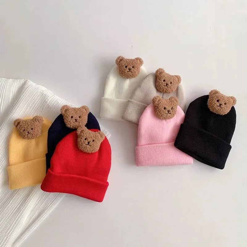 A collection of knitted baby hats in various colors, including yellow, black, pink, and gray, adorned with small brown bear e