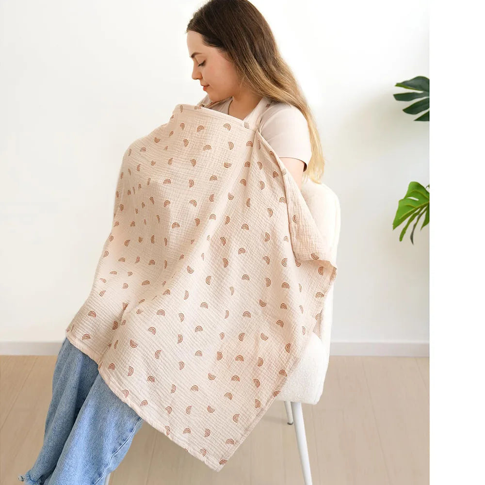 A woman is wearing a beige breathable muslin nursing cover with an adjustable neckline.