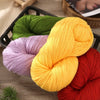 A collection of brightly colored yarn skeins, including green, purple, yellow, and red, displayed in a black basket.