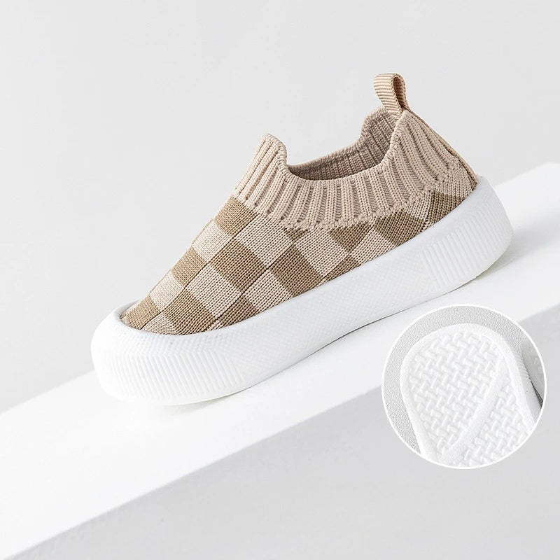 A pair of beige and tan plaid slip-on toddler shoes for first walkers, shown on a white surface.