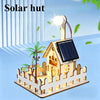 A wooden model kit of a solar hut with a solar panel and a light, set in a fenced outdoor scene.