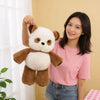 A young woman holds up a brown and white stuffed panda plushie against a light yellow background.