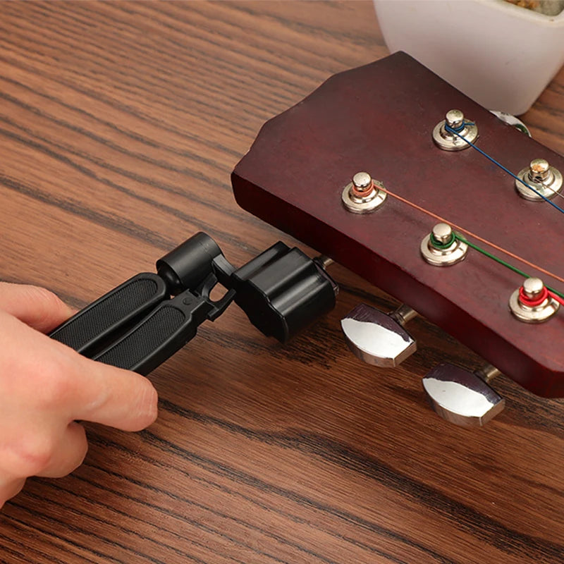 A hand is using a black tool to wind, cut, or pull guitar strings from a wooden fretboard.