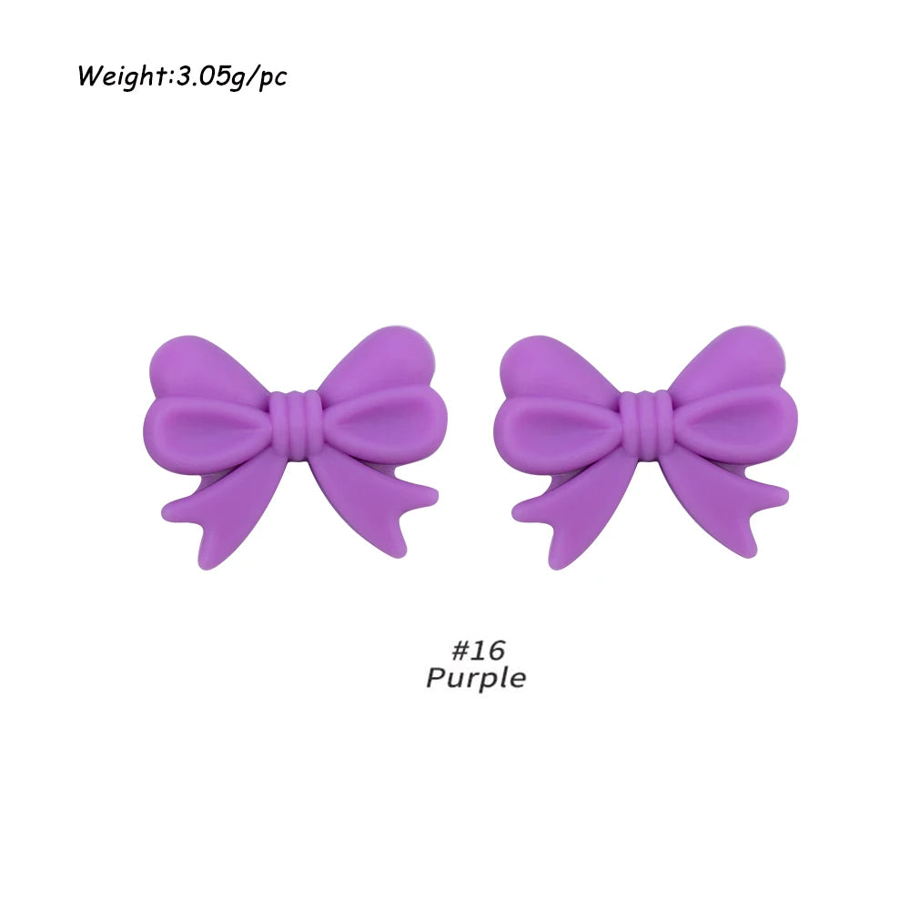 A pair of purple silicone bow tie beads used for jewelry making and craft projects.