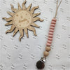 A wooden sun-shaped bead pacifier clip with a pink silicone teether on a twine string.