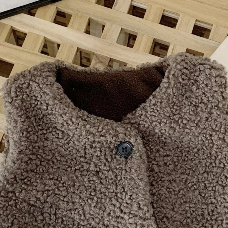 A close-up of a brown plush fleece vest for children, showing the texture and a dark button closure.