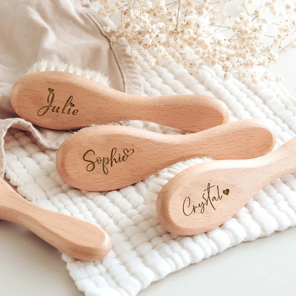 A set of three wooden baby brushes and combs with names Julie, Sophie, and Crystal engraved on them, resting on a white knitt