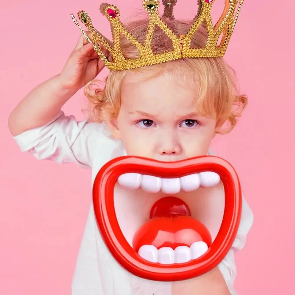 A toddler wearing a gold crown and a red mouth-shaped toy for fun voice changing