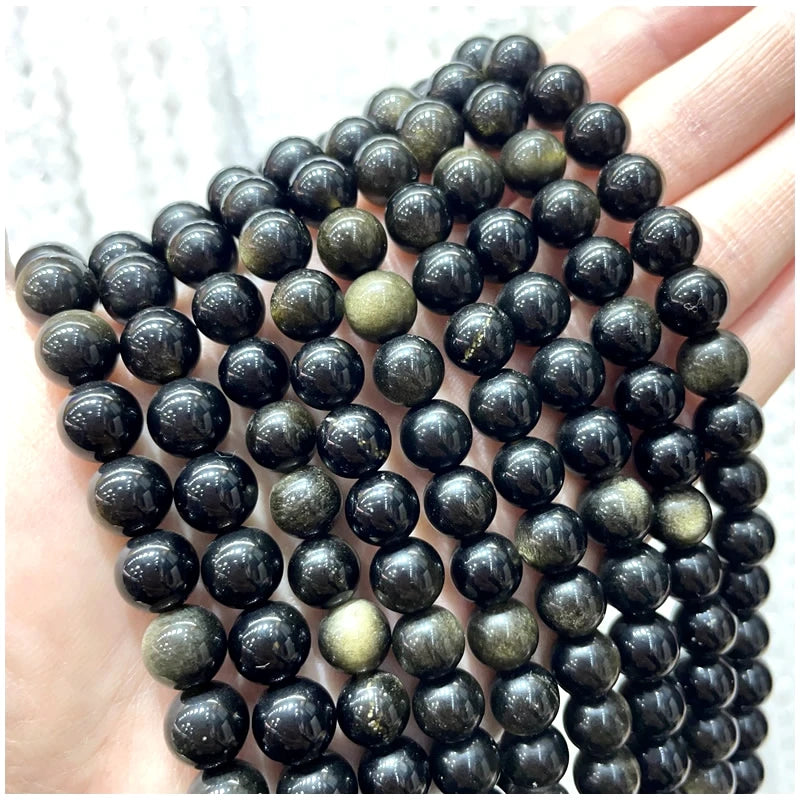 A hand holds a strand of dark, natural stone beads for DIY jewelry making.