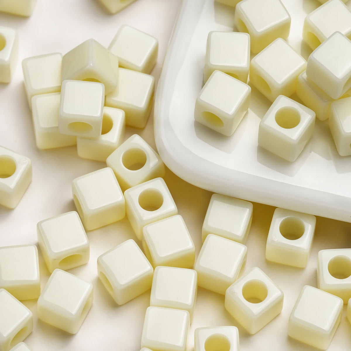A collection of white square acrylic spacer beads scattered on a white surface.
