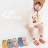 A child wearing a brown animal hood is sitting, with various cute cartoon animal non-slip socks laid out in front of them.