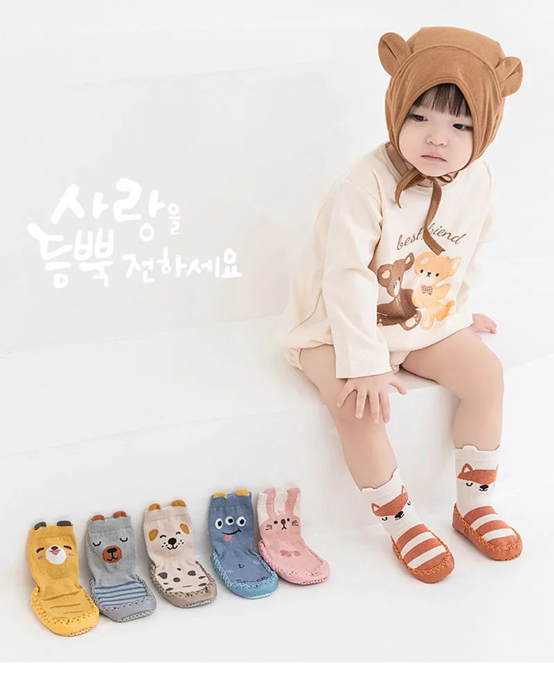 A child wearing a brown animal hood is sitting, with various cute cartoon animal non-slip socks laid out in front of them.