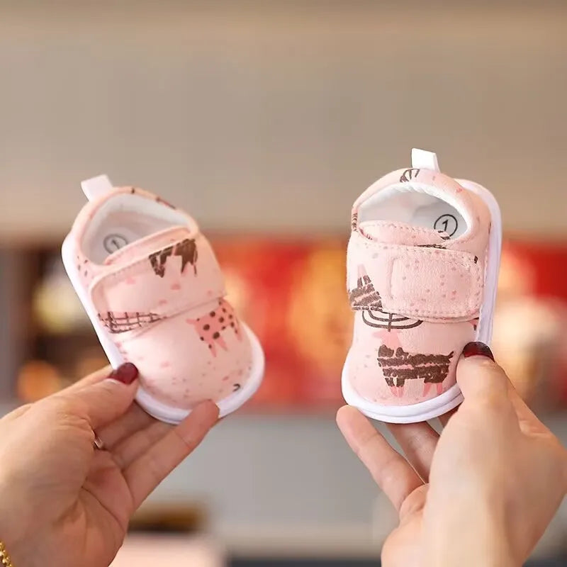 A pair of pink bear soft sole sandals for baby's first steps being held by a person.