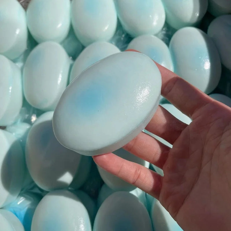 A hand holds a light blue, cheese-shaped squishy stress relief toy surrounded by similar items.