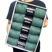 A box displaying a 5-pack of soft alpaca wool yarn in various shades of green.