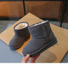 A pair of gray, fur-lined winter boots with a slip-on style are being held over a light brown surface.