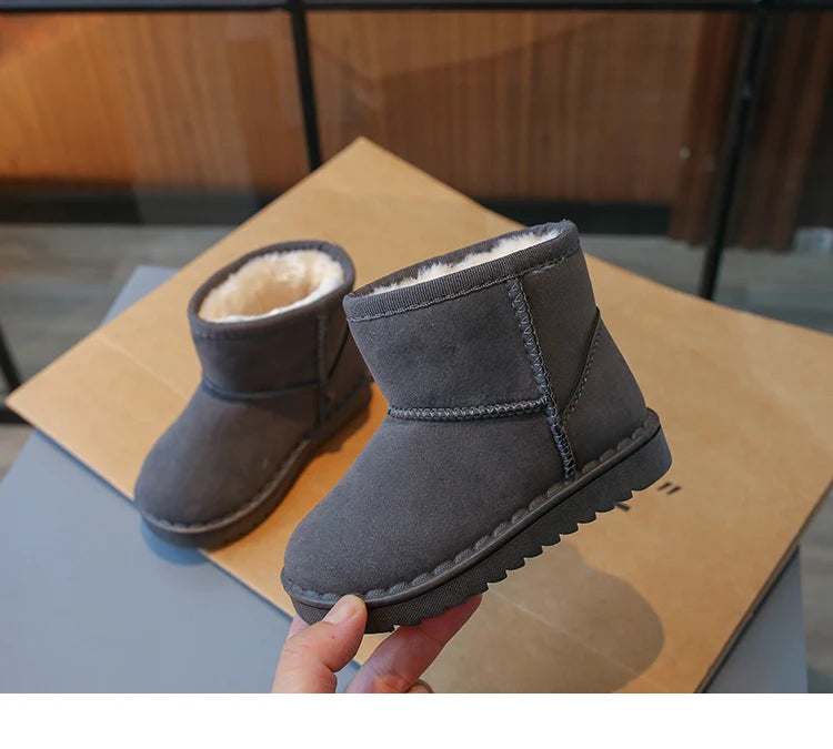 A pair of gray, fur-lined winter boots with a slip-on style are being held over a light brown surface.