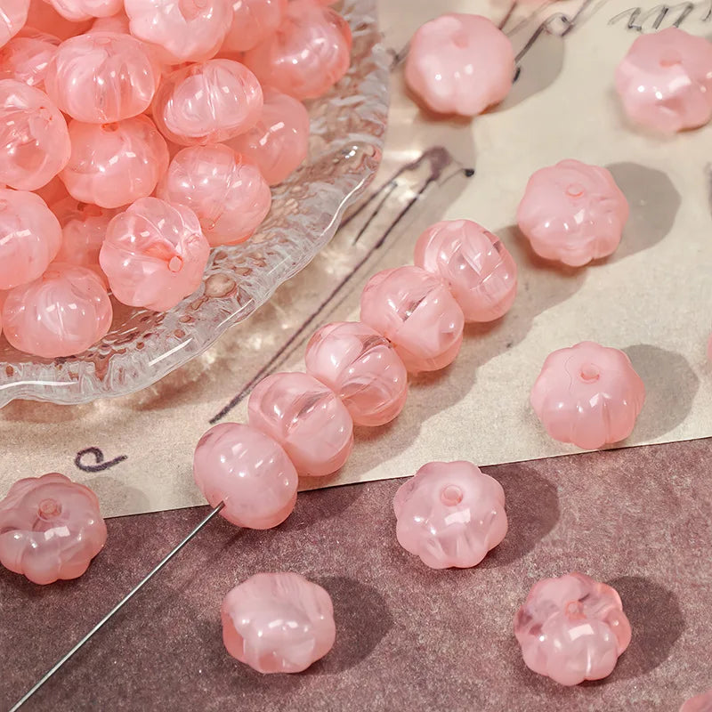 Pink gold-traced pumpkin resin beads scattered on a surface for jewelry making