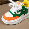 A close-up view of a white sneaker with green and orange accents and white laces