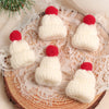 A set of mini knitted white hats with red pom-poms displayed on a lace fabric next to a pine branch.