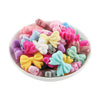 A bowl filled with colorful silicone bow tie beads in various shades of pink, purple, yellow, and blue for jewelry making.