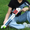 A person holds a white soft bullet shotgun toy with red shells and ejecting action in a grassy outdoor setting.
