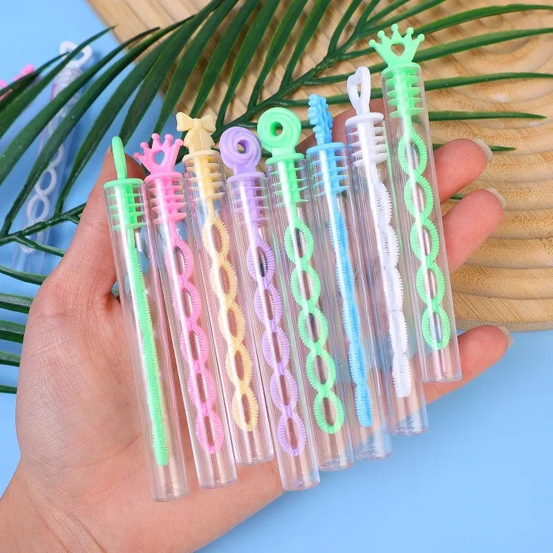 A hand holds a collection of colorful plastic bubble wands with 5-hole designs against a green palm leaf background.