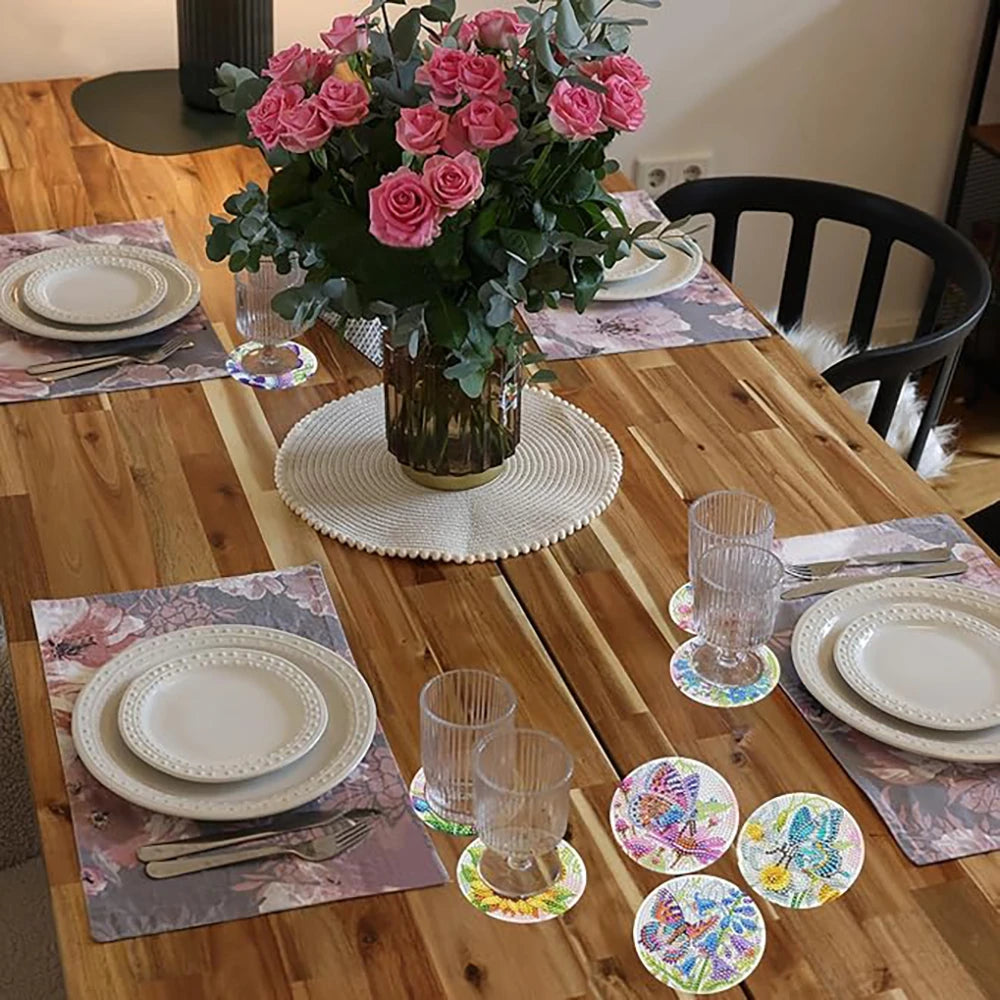 A floral arrangement of pink roses in a gold vase on a wooden table set for a meal.