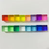 A row of colorful acrylic building blocks in a rainbow gradient, arranged horizontally.