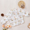 A white waterproof long sleeve feeding bib with a delicate floral pattern and a small stuffed rabbit decoration on a light be