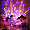 A family is gathered around a glowing disco ball light display in a dark room.