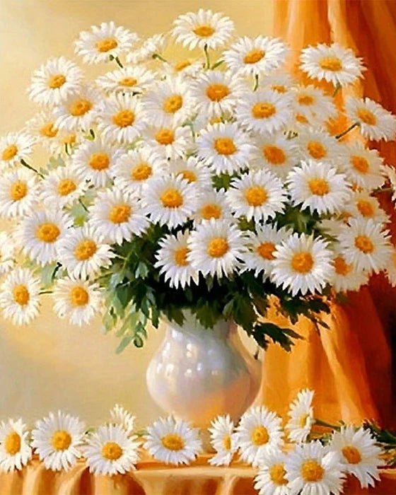 A bouquet of white daisies in a vase on a table with orange fabric backdrop.