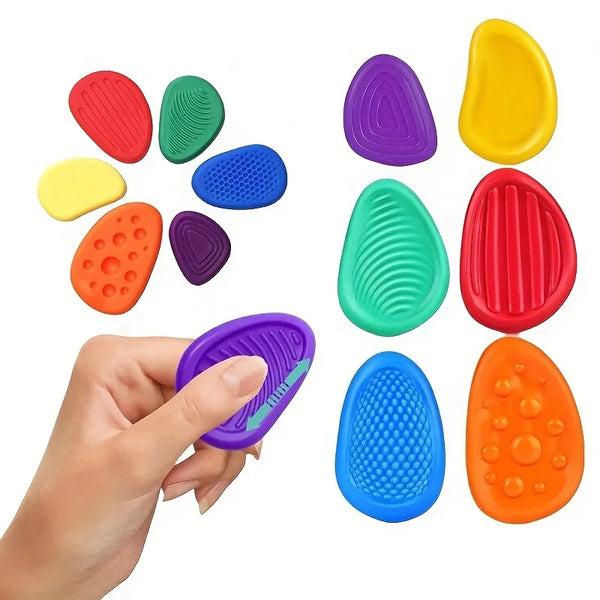 A hand holds a set of six colorful silicone sensory texture worry stones, including red, green, purple, yellow, and blue.