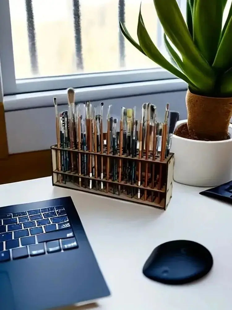 A wooden art brush and pencil organizer with 67 slots sits on a white desk next to a laptop.
