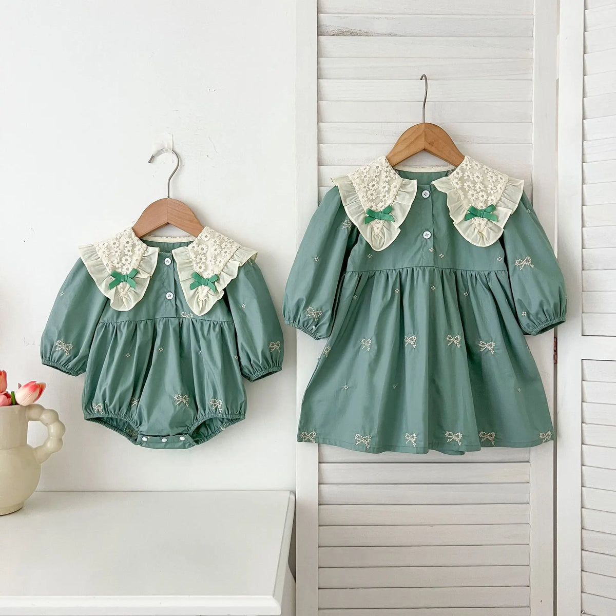 A teal cotton party dress for girls featuring lace collar details and embroidered accents, displayed on a hanger.