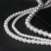 A strand of white acrylic pearl beads is laid out on a dark surface for jewelry making.