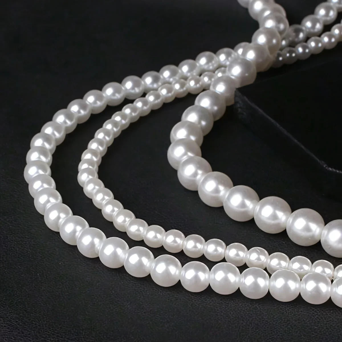 A strand of white acrylic pearl beads is laid out on a dark surface for jewelry making.