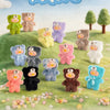 A collection of Teddy Mini figures in various colors and textures arranged on green grass under a blue sky.