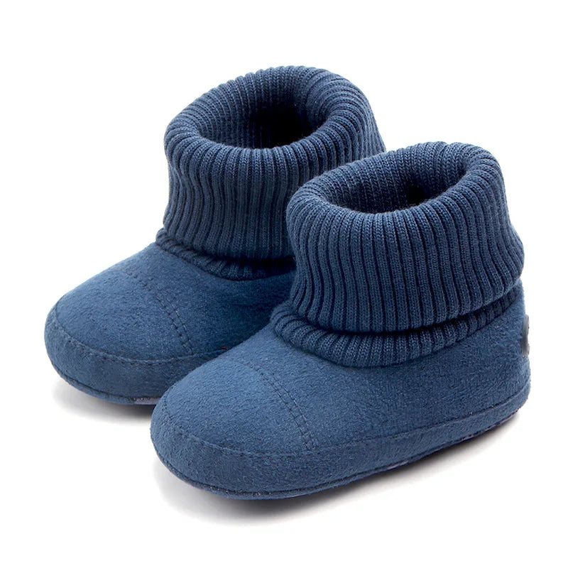 A pair of navy blue baby winter snow boots with ribbed cuffs and fuzzy ball accents.