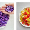 A hand holds a white dish filled with colorful nylon hair ties in purple and orange shades.