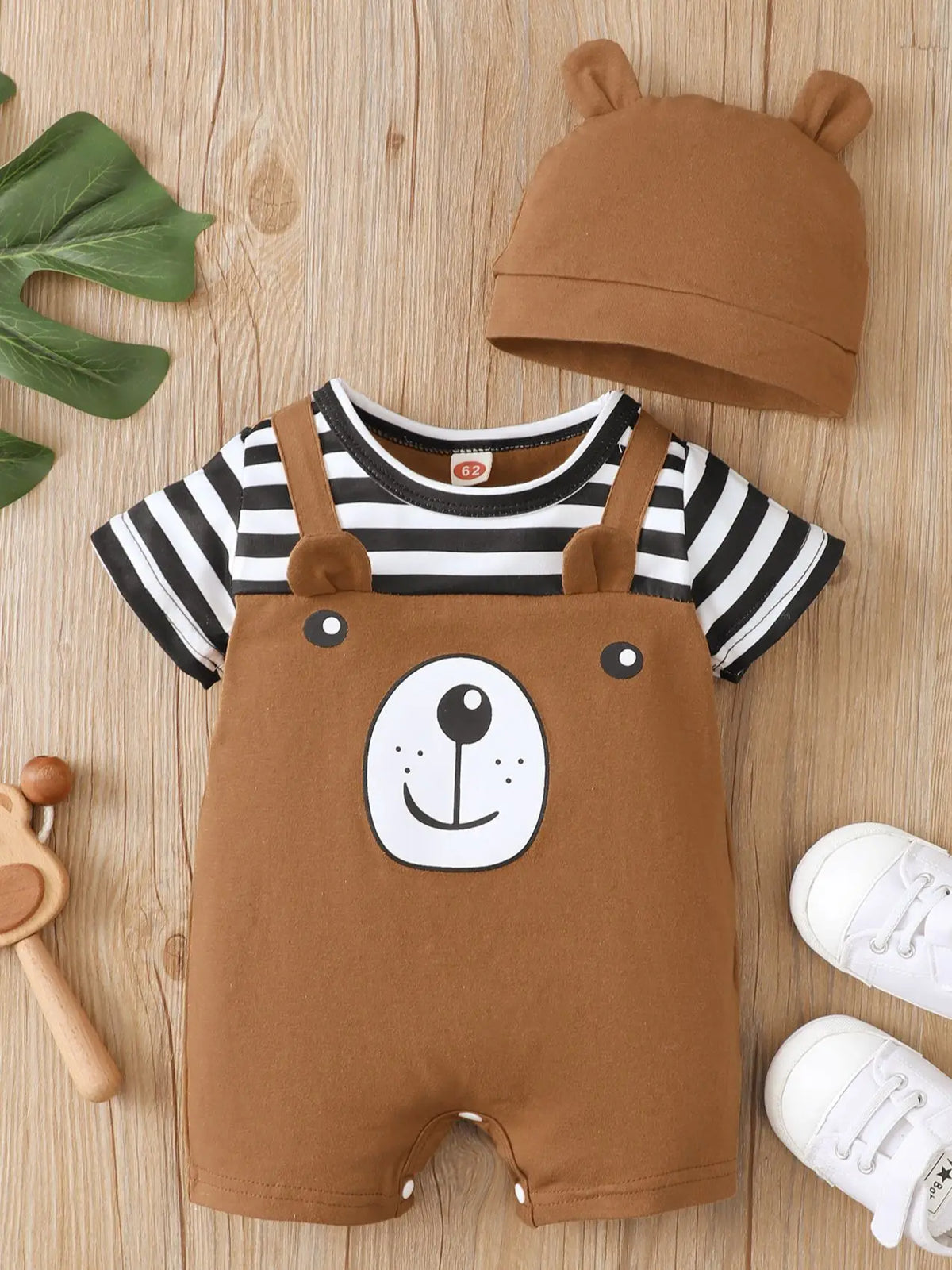 A brown baby bear print short sleeve romper and matching hat laid on a light wooden surface.