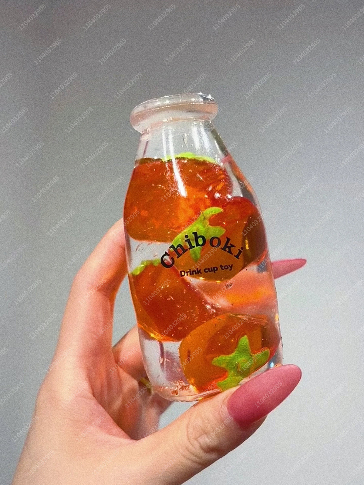 A hand holds a clear glass bottle filled with orange fruit pieces, serving as a drink cup toy.