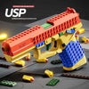 An assembled building block soft bullet gun toy in orange and yellow, shown on a gray surface with loose blocks.